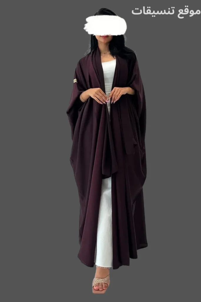 عباية بشت باللون العنابي الغامق مع قصة متدلية واسعة وتنسيق فستان أبيض تحته.