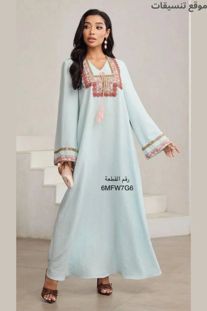 جلابية باللون الأزرق السماوي الفاتح، مزينة بتطريز وردي وقرميدي على الصدر والأكمام، مع شرابات (تاسل) متدلية من الياقة، قماش مكشكش خفيف.