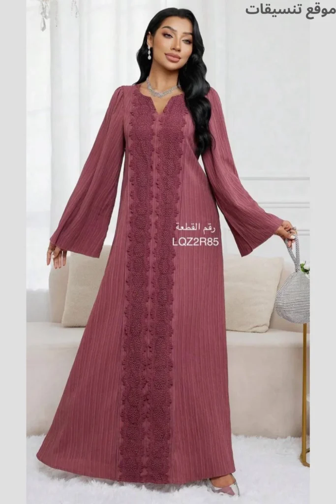 جلابية باللون العنابي الفاتح (التوتي)، مزينة بشريط دانتيل/كروشيه عامودي عريض في المنتصف، أكمام واسعة، قماش ذو ملمس محبب.