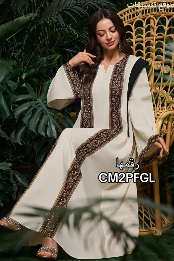 جلابية بلون بيج كريمي، مزينة بخطين عريضين من التطريز البني بنقوش نباتية تمتد طولياً من الأكتاف للأسفل، أكمام واسعة بحواف مطرزة.