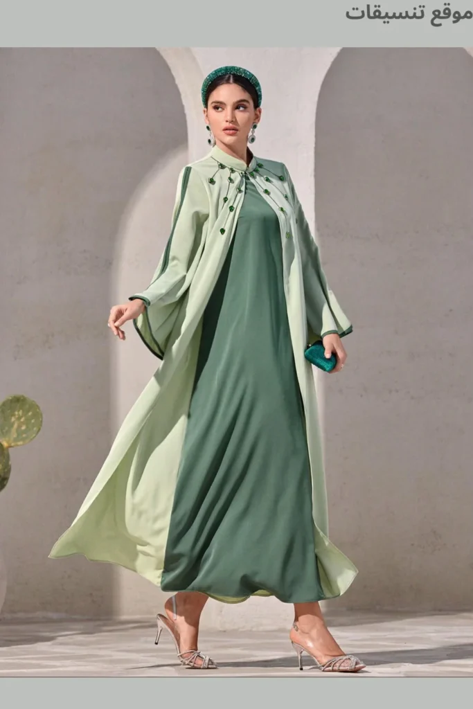 طقم جلابية يتكون من فستان داخلي أخضر زمردي غامق وعباية خارجية (كيب) بلون أخضر فاتح، مزينة بتطريز كريستالات خضراء عند الرقبة.